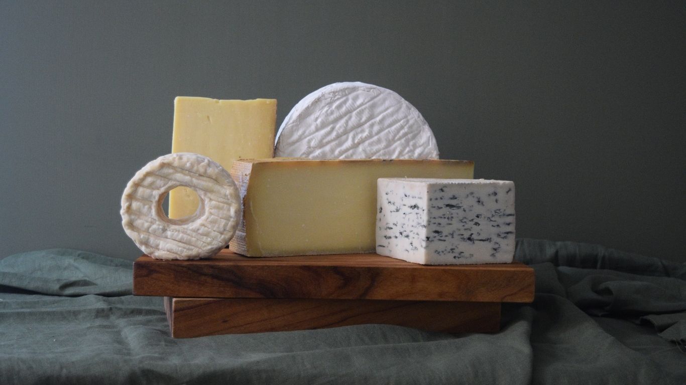 Assorted types of cheese on a wooden board with a dark background