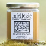 The Artisan Cheese Room Miellerie Leatherwood unheated honey in a 325g glass jar resting on a mossy forest surface.
